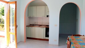 A kitchen with white cabinets, a sink, and a dining table with a colorful tablecloth. - Santa Chiara Hotel Residence (Ricadi)
