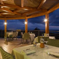 Un espacio de comedor al aire libre con mesas y sillas, techo de madera y vista al agua.