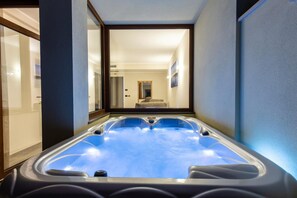 Een moderne spa-ruimte met een ruime hot tub, een glazen deur naar een slaapkamer en uitzicht op de gang.