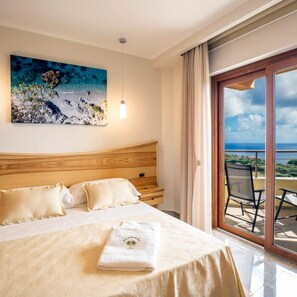 A hotel room with a bed, a painting, a balcony with a chair, and a view of the sea. - Santa Chiara Hotel Residence (Ricadi)