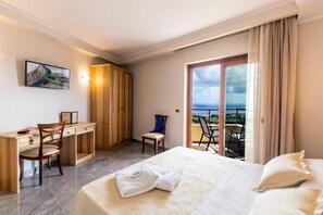 Hotellihuone, jossa on sänky, työpöytä, tuoli, parveke, jolta on näkymä, ja seinällä riikinkukkoaiheinen taulu.