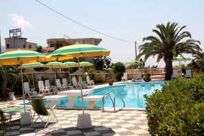 Ein Hotelpoolbereich mit mehreren Liegestühlen und Sonnenschirmen, einem Schwimmbecken und einer Palme.
