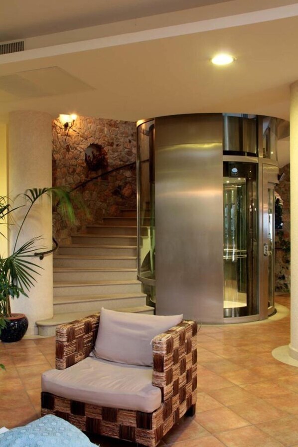 Eine Lobby mit einer geschwungenen Treppe, einem Glastunnel, einem Korbstuhl und einem Blumentopf.