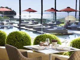 Comedor con una mesa dispuesta para dos, con vista a una piscina con sillones y sombrillas.