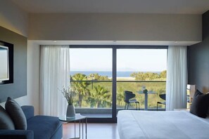 Un dormitorio con una cama grande, un sofá, una mesita y un balcón con vista a la playa.