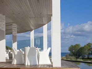A modern outdoor seating area with white furniture, large glass windows, and a view of the sea. - Aqua Blu Boutique Hotel and Spa - Adults Only (Kos)