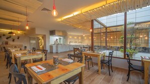 A restaurant with wooden tables and chairs, a kitchen area, and large windows offering a view. - Portblue Le Sivory Boutique Hotel (Punta Cana)