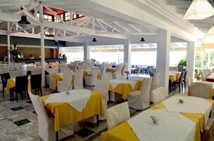 Un amplio comedor interior con mesas cubiertas de manteles amarillos, sillas blancas y un techo alto con vigas a la vista.