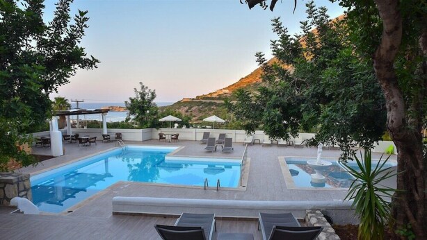 A pool area with lounge chairs and umbrellas, surrounded by trees and overlooking a hilly landscape. - Bali Mare (Mylopotamos)