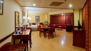 A hotel room with a dining area, a sofa, a TV, and a curtain.