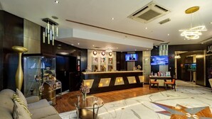 A modern hotel lobby with a reception desk, seating area, and a large screen displaying a program.