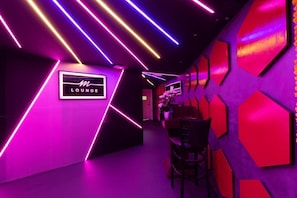Um lounge moderno com iluminação neon, uma placa com a palavra 'Lounge' e uma área de estar com cadeiras.