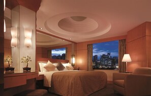 Une chambre d’hôtel équipée d’un lit, d’un bureau, d’une chaise, d’une grande fenêtre donnant sur la ville et d’un éclairage fixé au mur.