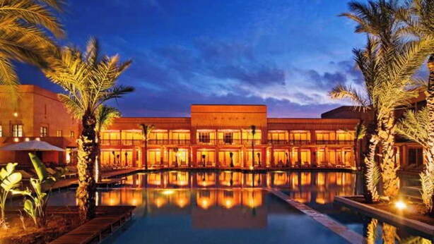Un hôtel doté d’une piscine, de palmiers et dont le reflet se mire dans l’eau.