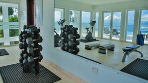 A gym with exercise equipment, a large mirror, and a view of the ocean through large windows. - Xeliter Vista Mare (Samaná)