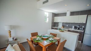 A modern kitchen with white cabinets, a dining area with a glass table, and a small island with a sink. - Xeliter Vista Mare (Samaná)