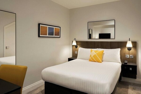 A hotel room with a large bed, two bedside tables, a chair, a framed picture, and a mirror on the wall. - Best Western Kensington Olympia Hotel (London)
