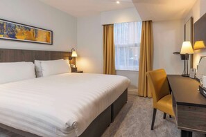A hotel room with a large bed, a desk, a chair, a lamp, and a painting on the wall. - Best Western Kensington Olympia Hotel (London)