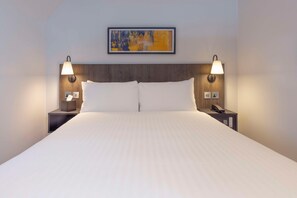 A hotel room with a large bed, two bedside lamps, a nightstand with a phone, and a painting on the wall. - Best Western Kensington Olympia Hotel (London)