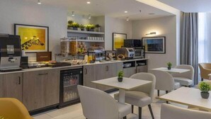Moderni hotellihuone, jossa on pieni keittiö, ruokailutila ja suuri ikkuna, jossa on verhot.