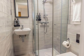A modern bathroom with a glass-enclosed shower, a white sink, and toiletries on a shelf. - Best Western Kensington Olympia Hotel (London)