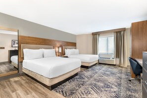 A hotel room with two beds, a desk, a chair, a mirror, and a large window with curtains.