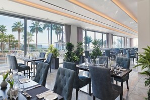 A modern dining area with tables set for two, large windows, and potted plants. - St. George Beach Hotel & Spa Resort - Adults Only (Chlorakas)
