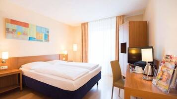 Ein Hotelzimmer mit Bett, Schreibtisch mit Stuhl, Fernseher und Zeitschriftenständer.