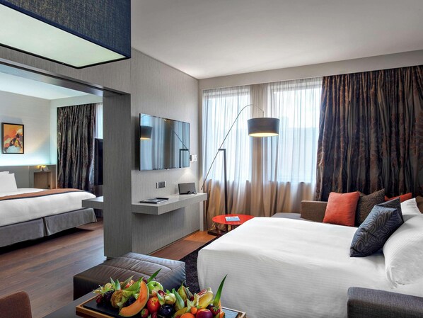 Una habitación de hotel moderna con una cama grande, un escritorio con una computadora portátil, un televisor de pantalla plana montado en la pared y un frutero en la mesita de noche.