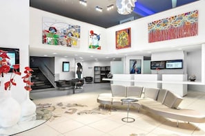 A modern hotel lobby with a reception desk, seating area, artwork on the walls, and a staircase leading to another level. - Firstname Toulouse - JDV by Hyatt (Toulouse)