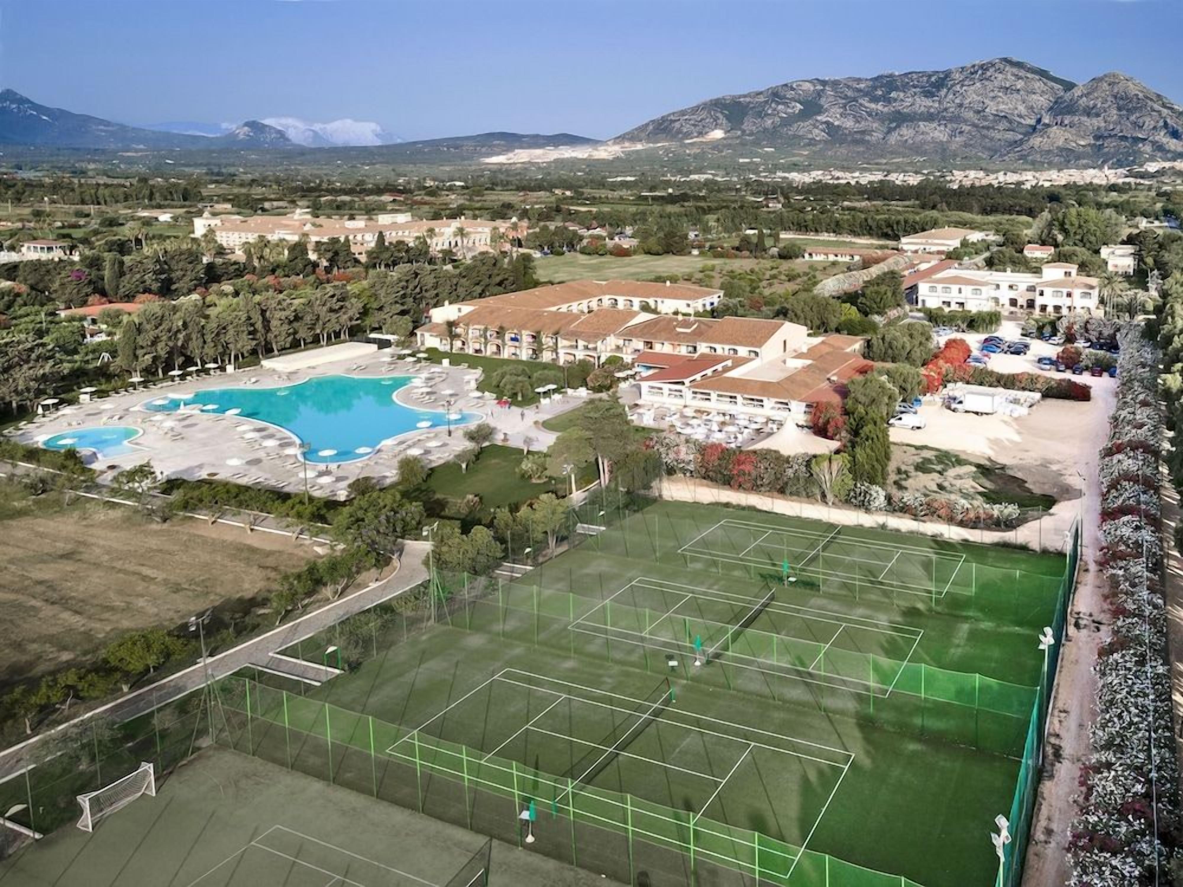 A resort with a swimming pool, tennis courts, and a mountain backdrop.