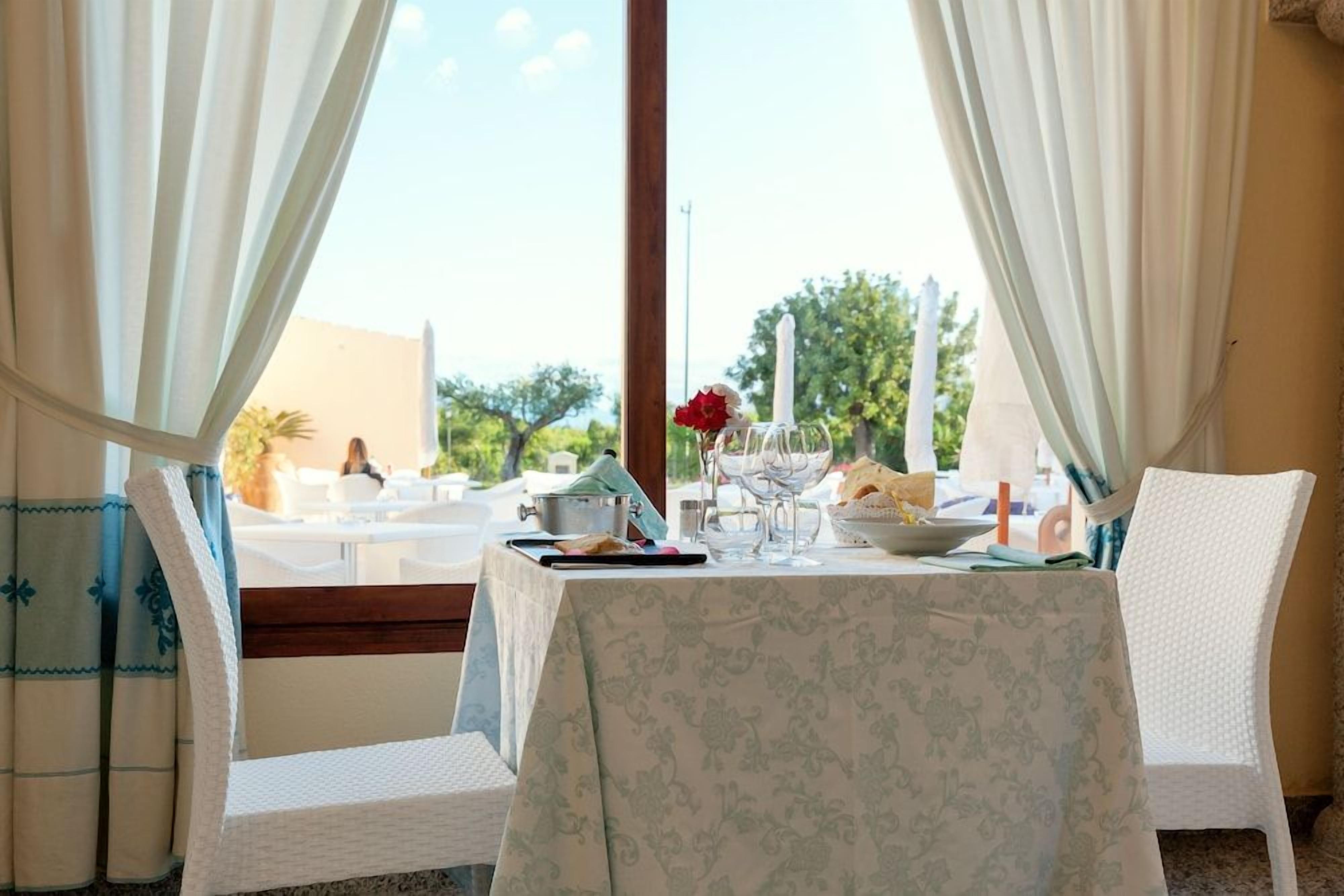 A dining table with a floral tablecloth, white chairs, and a view of the outdoors.