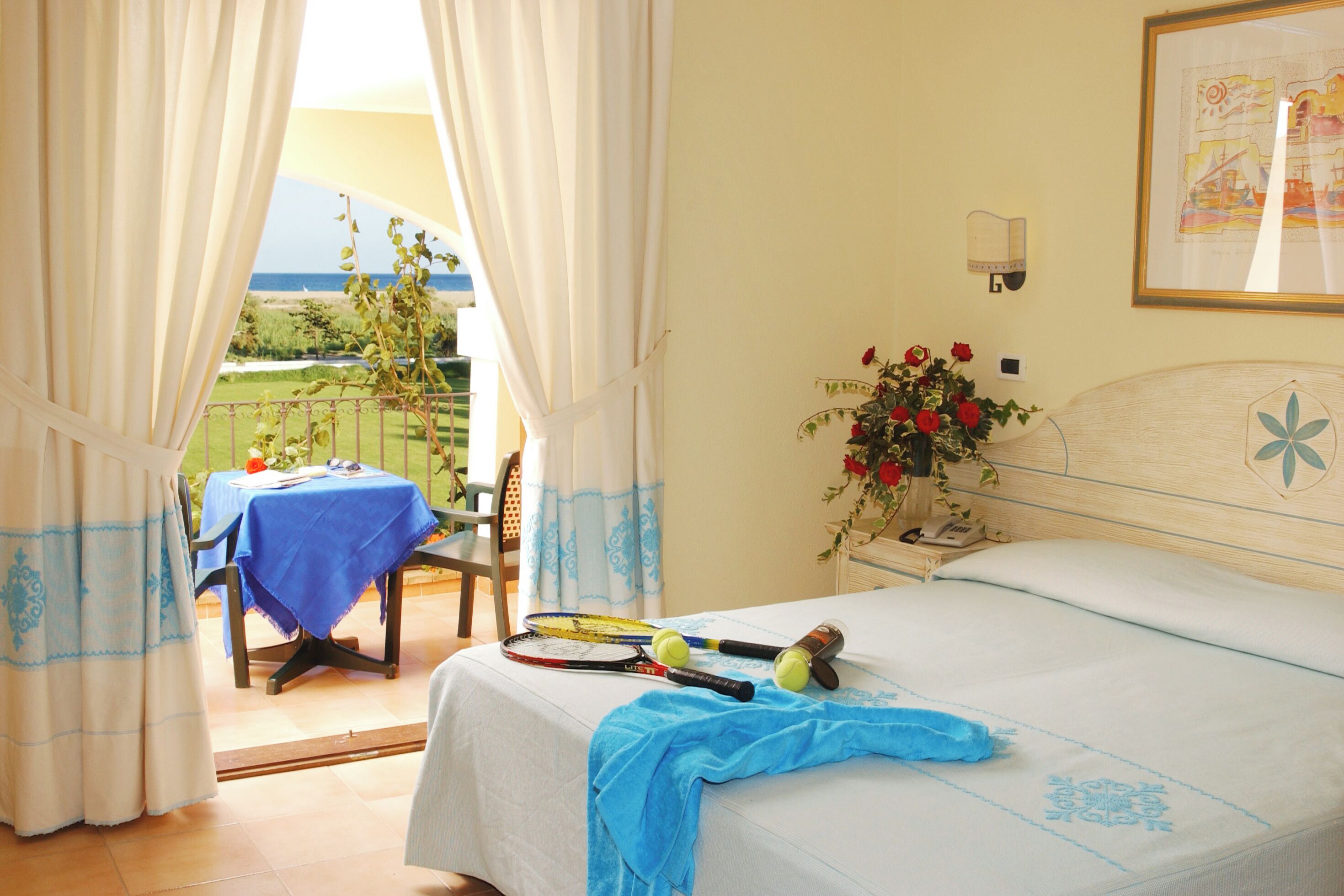 A bedroom with a bed, a table with a blue tablecloth, and a view of the outdoors.