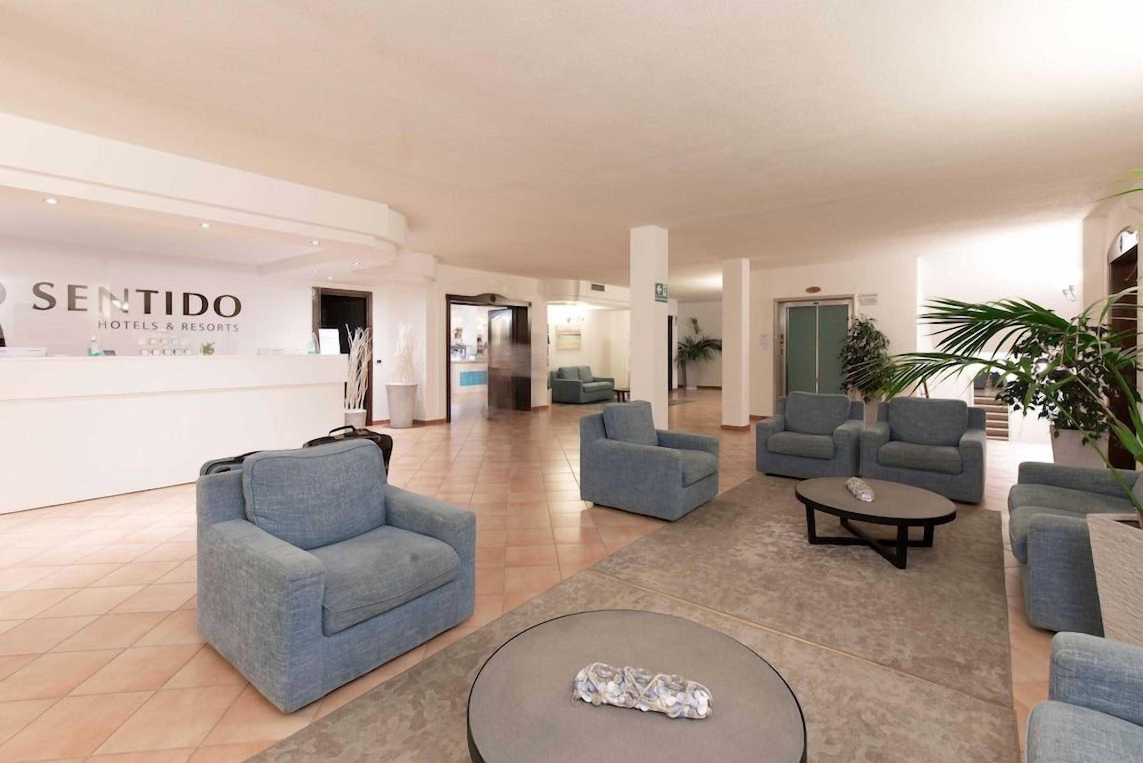 A hotel lobby with a reception desk, multiple seating areas, and a staircase in the background.