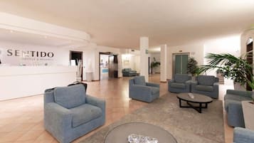 A hotel lobby with a reception desk, multiple seating areas, and a staircase in the background.