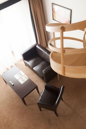 Ein Hotelzimmer mit einer schwarzen Ledersofa, einem kleinen schwarzen Sessel, einem Holzbeistelltisch und einem runden Holztisch.