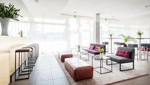A modern hotel lobby with a row of bar stools, a sofa, and a coffee table. - Azimut Hotel Munich (Munich)