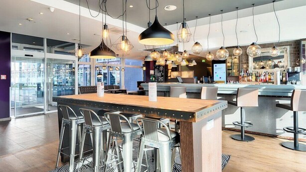 A modern bar area with a central island, bar stools, hanging pendant lights, and a visible bar counter. - Azimut Hotel Munich (Munich)