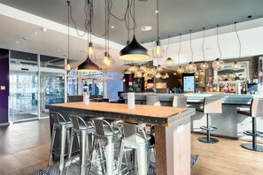 Uma área de bar moderna com ilha central, banquetas, luminárias pendentes e balcão de bar à mostra.