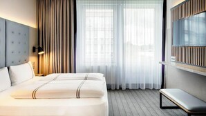 A hotel room with a large bed, a bench, a TV, and a window with curtains. - Azimut Hotel Munich (Munich)