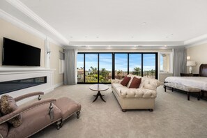 Ein geräumiges Wohnzimmer mit einem großen Flachbildfernseher, einem beige farbenen Sofa, einem braunen Sessel, einem runden Couchtisch und einem Bett mit Holz-Kopfteil.