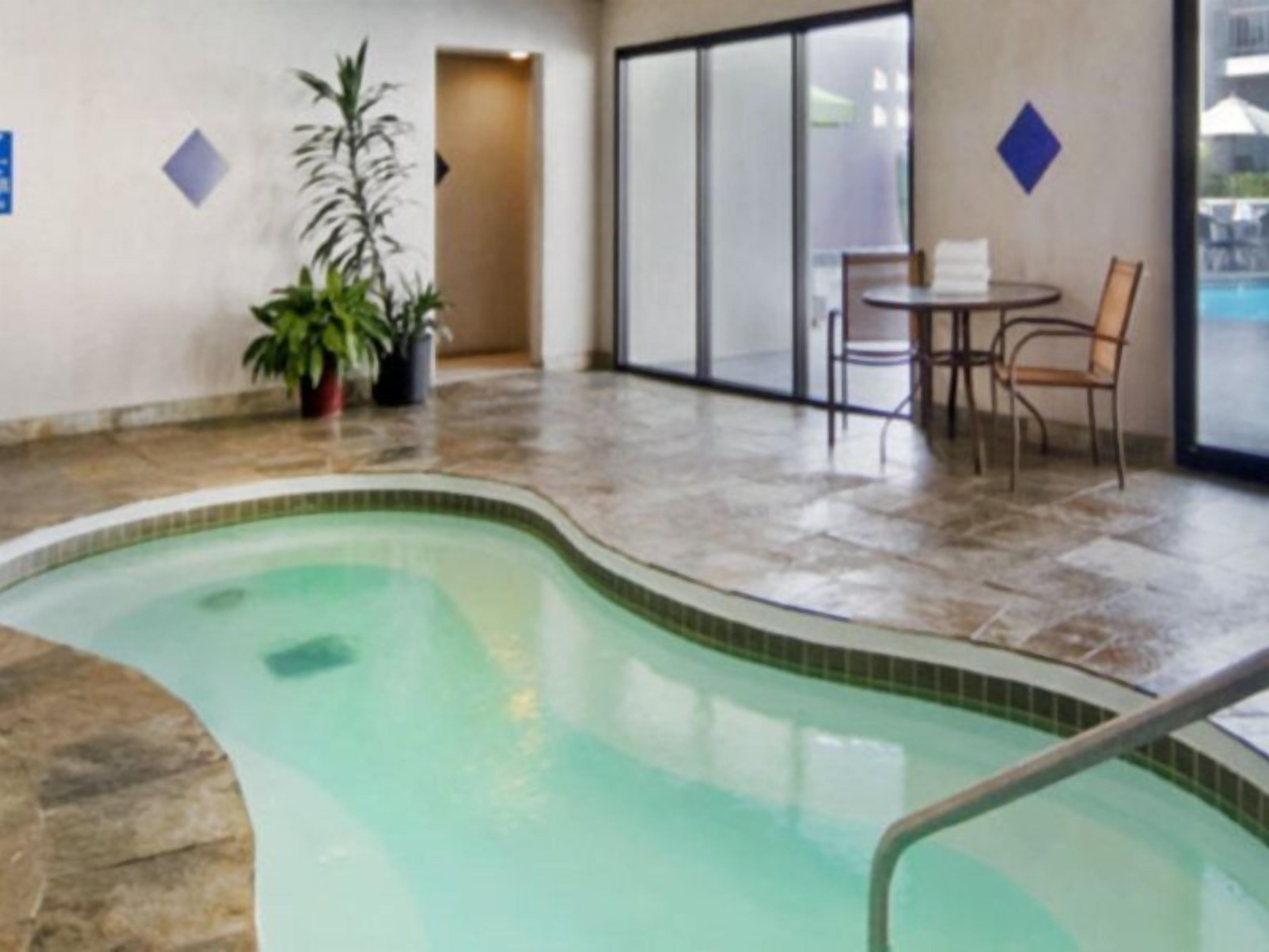 A swimming pool with a tiled deck, a potted plant, and a seating area with chairs and a table.