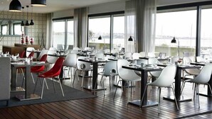 A modern dining area with tables and chairs, large windows, and a view of the city. - Pestana Cidadela Cascais (Cascais)