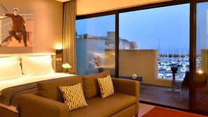 A hotel room with a bed, a sofa, a large window with a view of boats, and a painting on the wall. - Pestana Cidadela Cascais (Cascais)