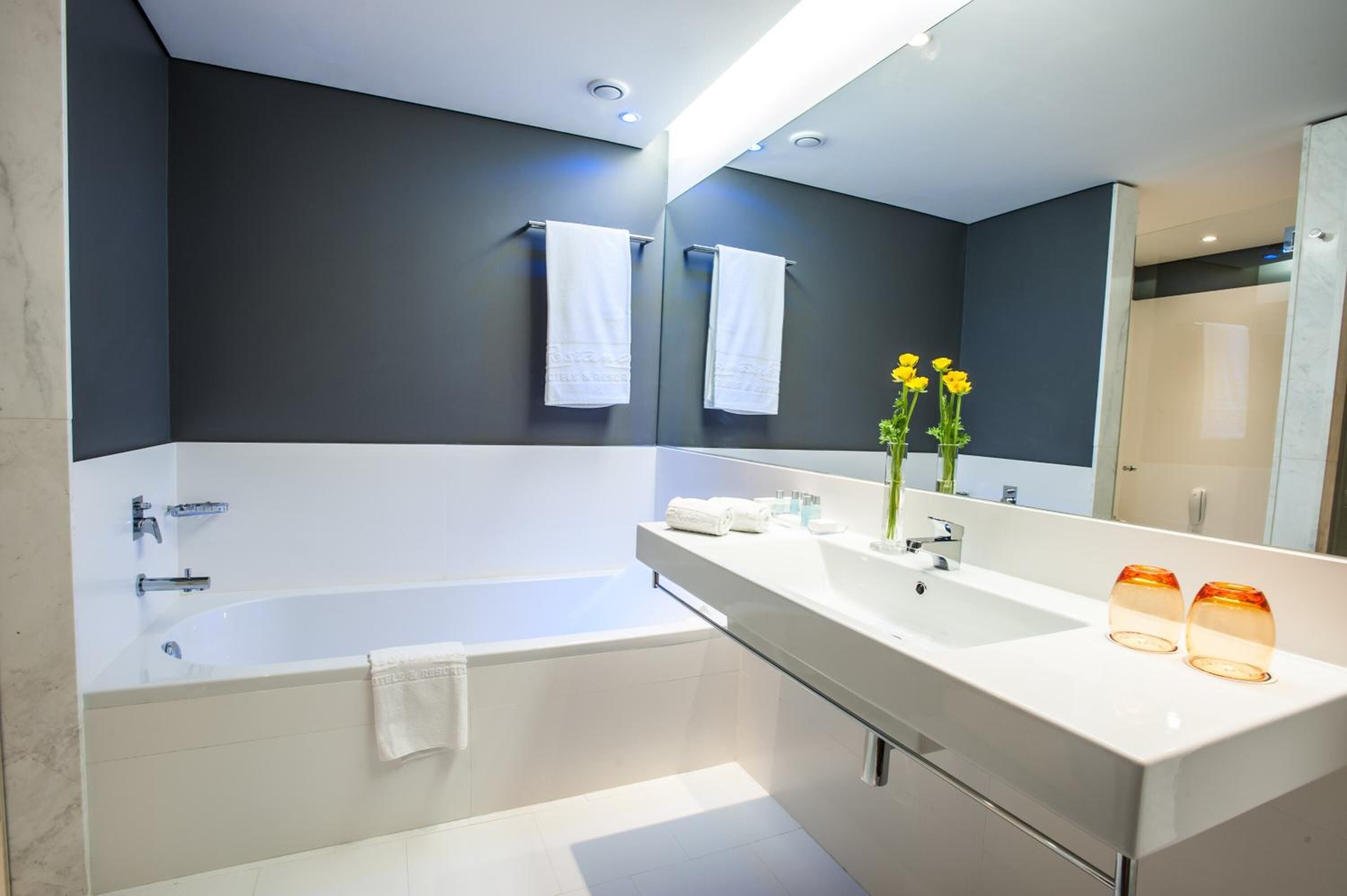 Een moderne badkamer met een badkuip, een grote spiegel en een wastafelmeubel met een wastafel en twee glazen kandelaars.