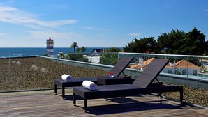 A deck with two lounge chairs, a small table, and a view of the sea and a lighthouse. - Pestana Cidadela Cascais (Cascais)