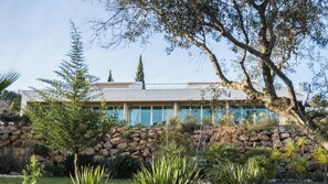 A modern building with a stone facade, large windows, and a well-maintained garden with various plants and a rock wall. - Vila Valverde Design and Country Hotel (Lagos)