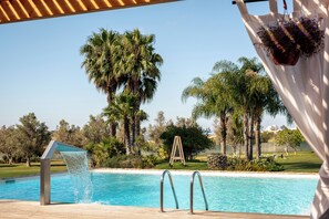 A swimming pool with a wooden deck, surrounded by palm trees and a grassy area. - Vila Valverde Design and Country Hotel (Lagos)
