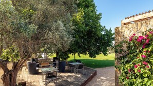 An outdoor patio area with a wooden deck, wicker furniture, and a stone wall with flowering plants. - Vila Valverde Design and Country Hotel (Lagos)