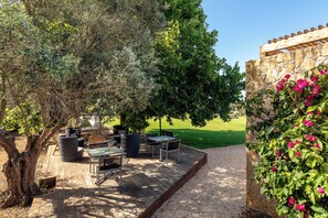 An outdoor patio area with a wooden deck, wicker furniture, and a stone wall with flowering plants. - Vila Valverde Design and Country Hotel (Lagos)